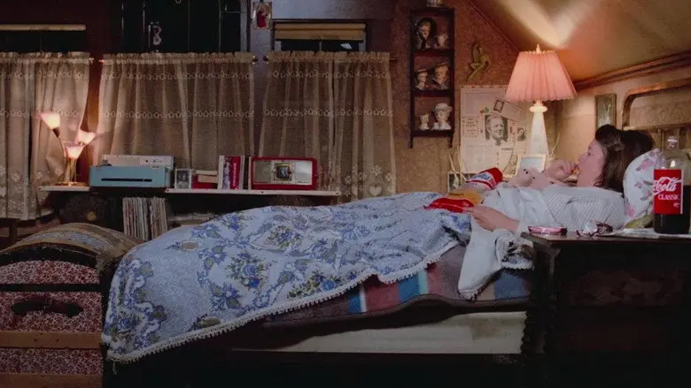 A woman lying in a quilted bed in a room filled with personal objects