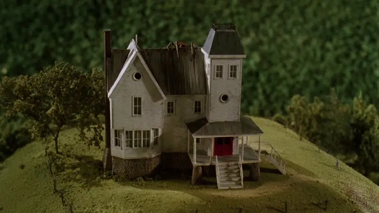 A miniature white house with a red front door on a grassy hill