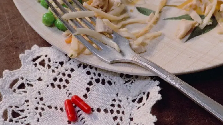 Two red capsules beside a plate and fork on a lace table covering