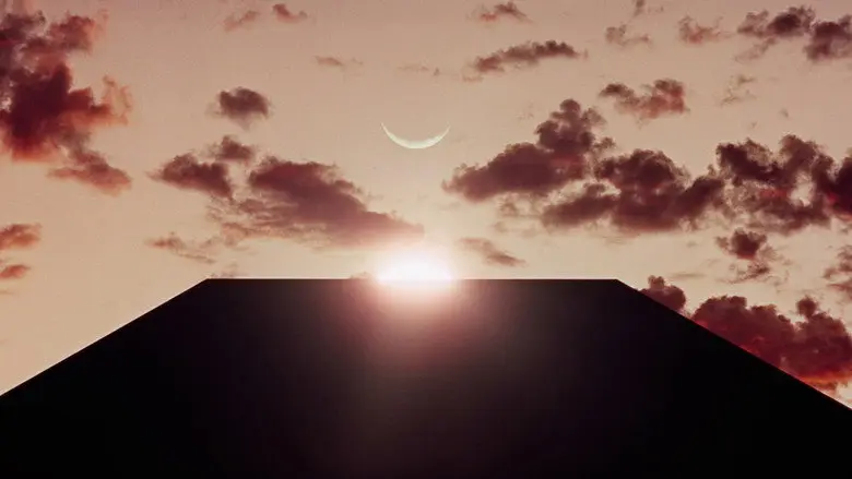 A black monolith rising above a dark landscape beneath a crescent moon and sunrise in 2001: A Space Odyssey