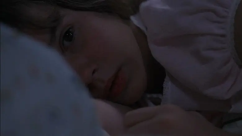 Regan lying on a pillow in a dark bedroom in The Exorcist