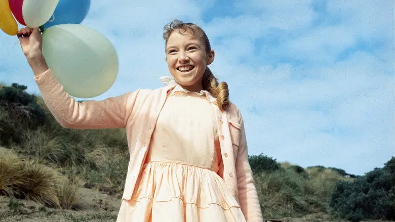 A child holding colorful balloons in front of a bright blue sky