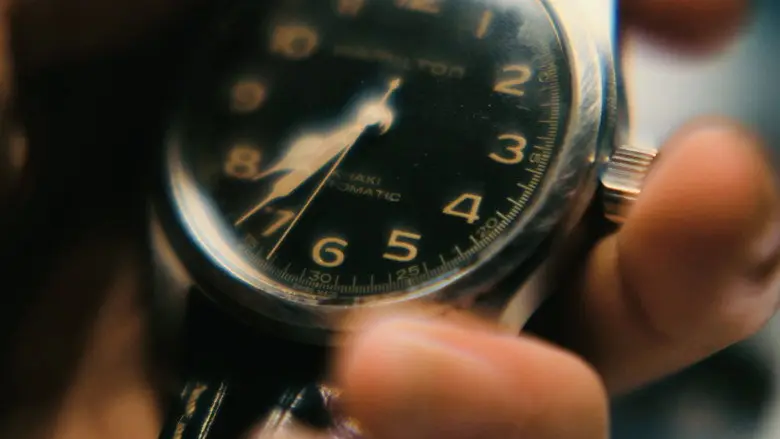 A hand holding a watch with a dark face in Interstellar