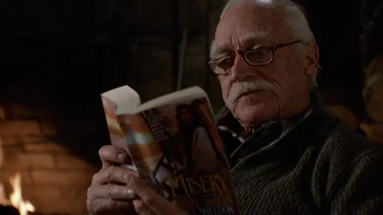 An older man reading a paperback titled Misery