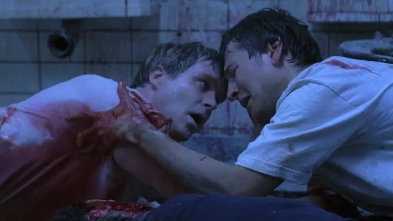 Two men facing each other in blue bathroom light in Saw