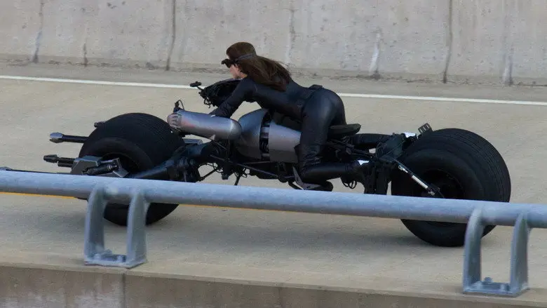 Catwoman rides the Batpod beside a concrete barrier in The Dark Knight Rises