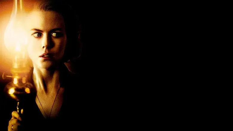 A woman holding a candle as her face emerges from darkness in The Others