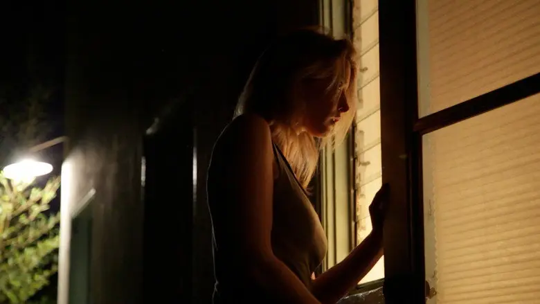 A woman standing beside a lit doorway at night in Coherence