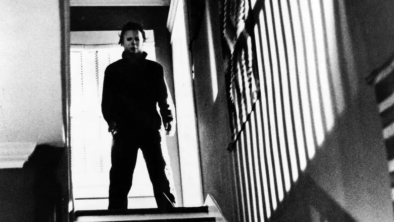 A masked figure near a doorway and hard vertical shadows in Halloween