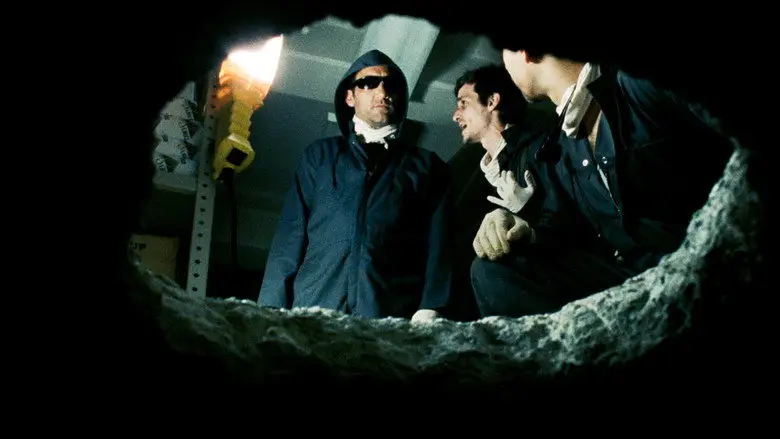 Three masked figures in dark hooded clothing behind bank-vault bars in Inside Man