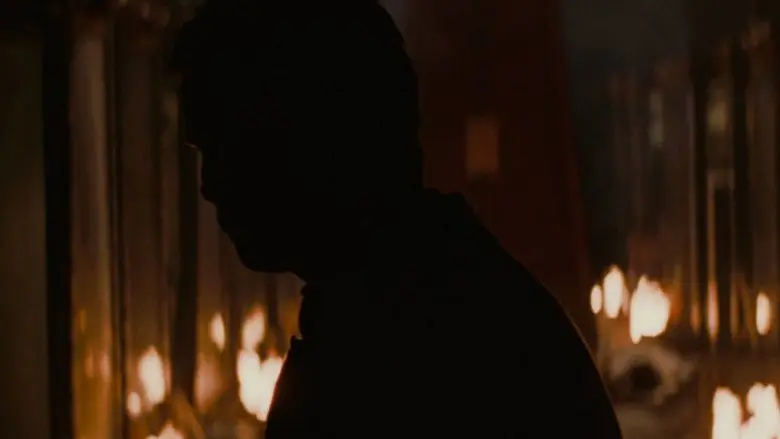 A man's silhouette in a dark room lit by small flames in The Prestige