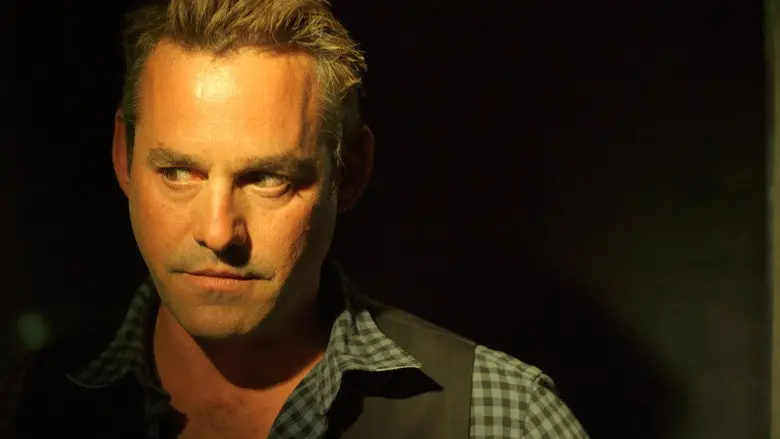 A man in a checkered shirt seen in low light in Coherence