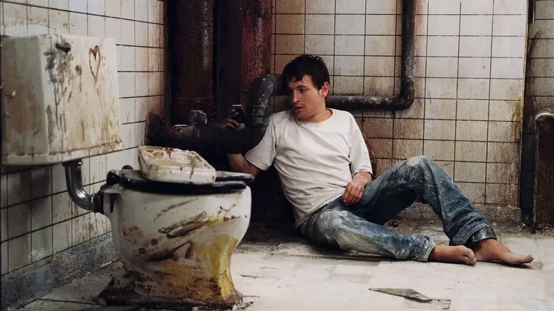 A man seated beside a toilet in the filthy bathroom from Saw