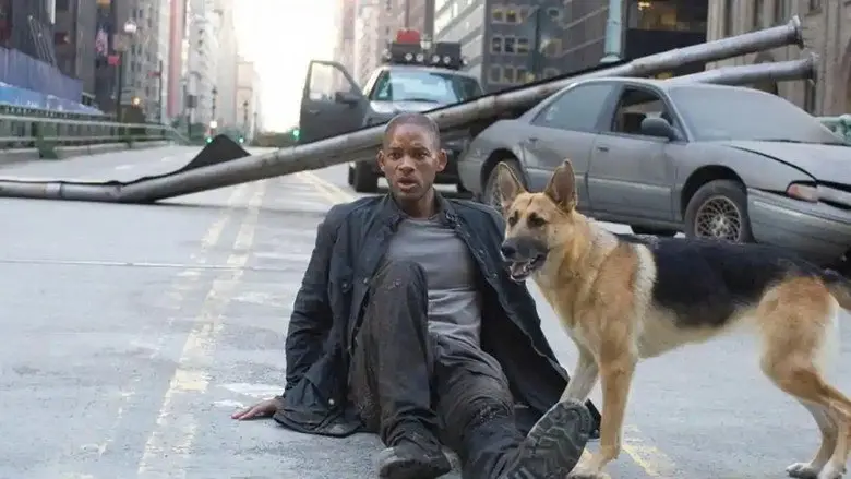 Robert Neville sitting on a city street beside his German shepherd amid damaged vehicles in I Am Legend